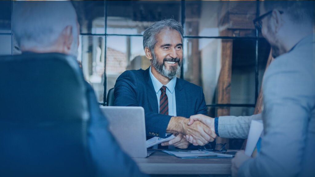 Two business professionals shaking hands across a desk to finalize a partnership with an appointment setting agency.